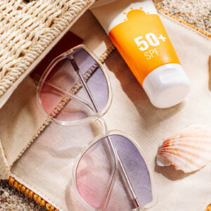 Sunscreen and glasses in a wicker straw bag on a sandy beach